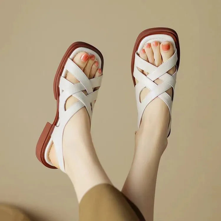 Women's black patent leather square toe sandals with cross strap design on a beach background
