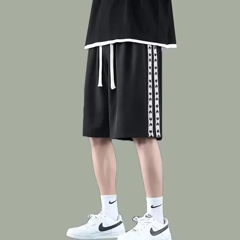 Man wearing loose fit black track pants with an elastic waistband, casual sports style.