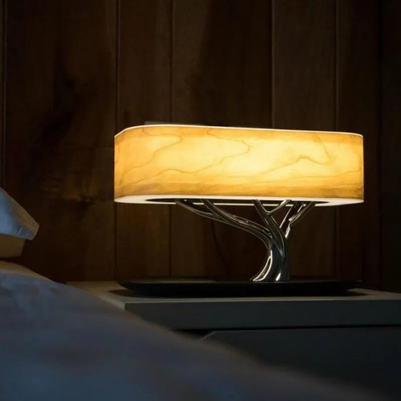 Creative tree light table lamp with natural cherry veneer shade, Bluetooth speaker, and wireless charging on a bedside table