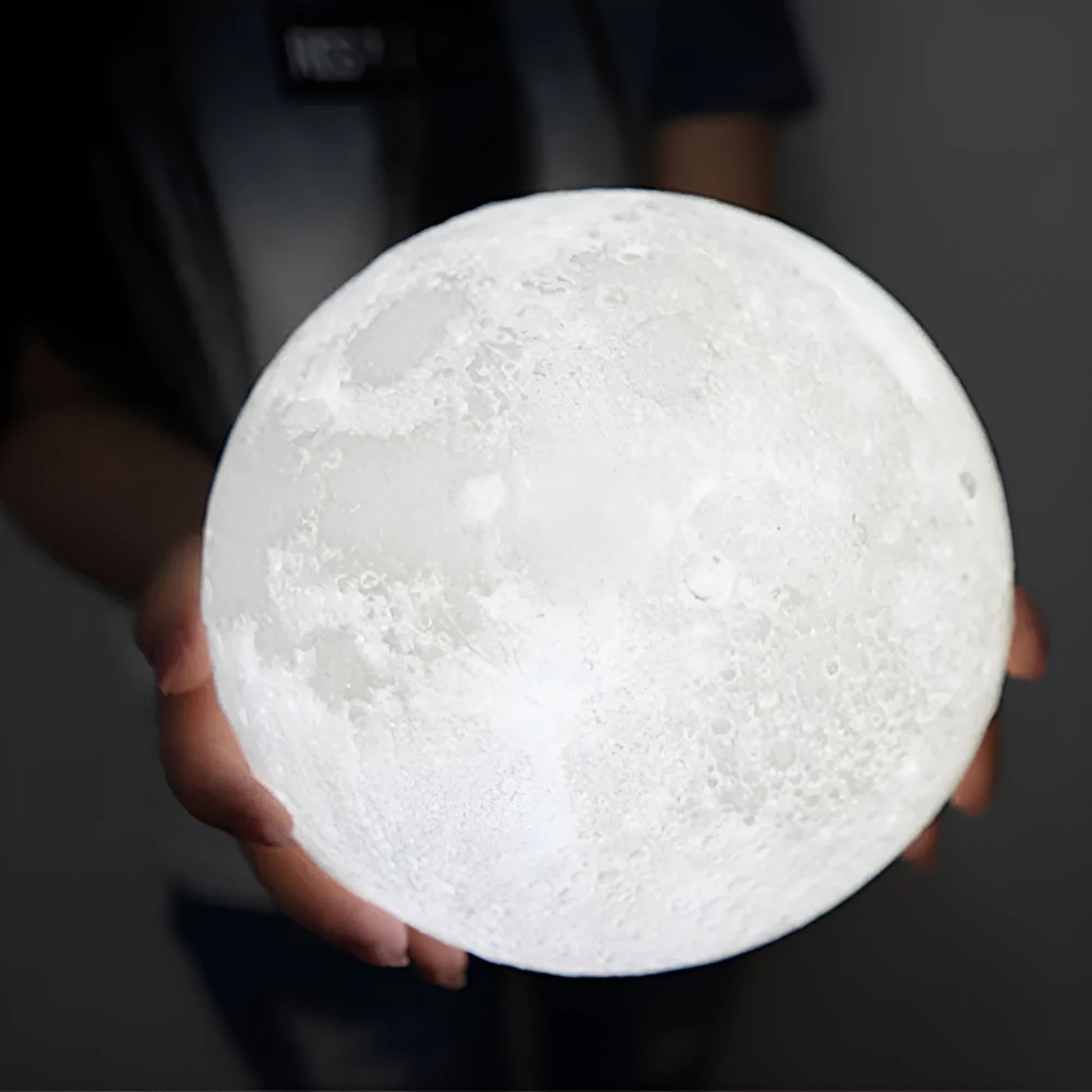 3D printed spherical moon lamp with textured surface on a wooden stand, showing white LED light.