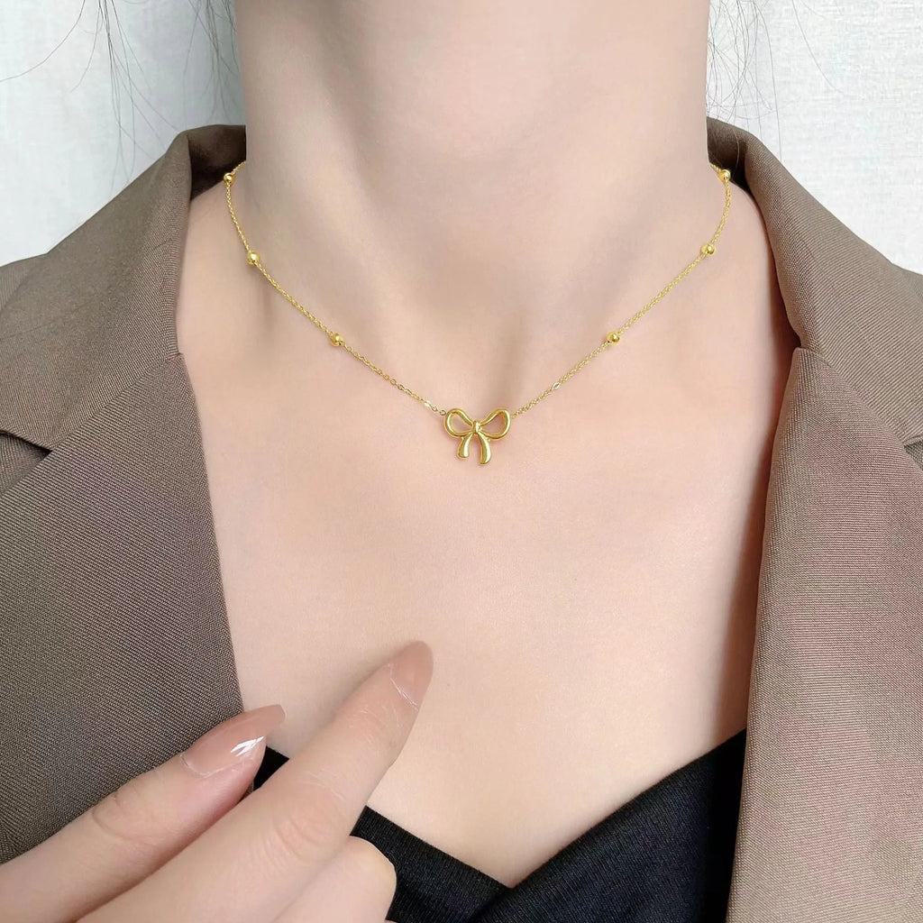Gold electroplated bow design necklace with cross chain on white background