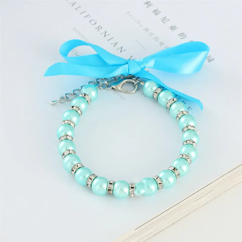 Small dog wearing adjustable pearl and rhinestone necklace with soft ribbon bow in blue colour