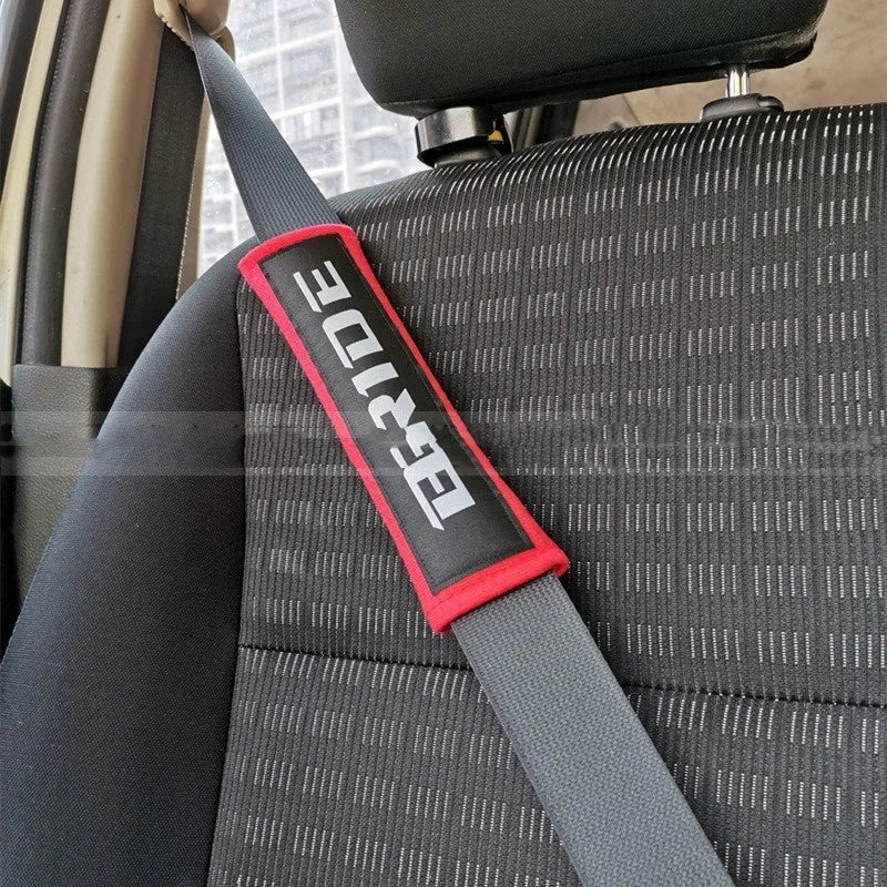 Pair of black cotton seat belt shoulder sleeves with embroidery, shown next to a car seat.