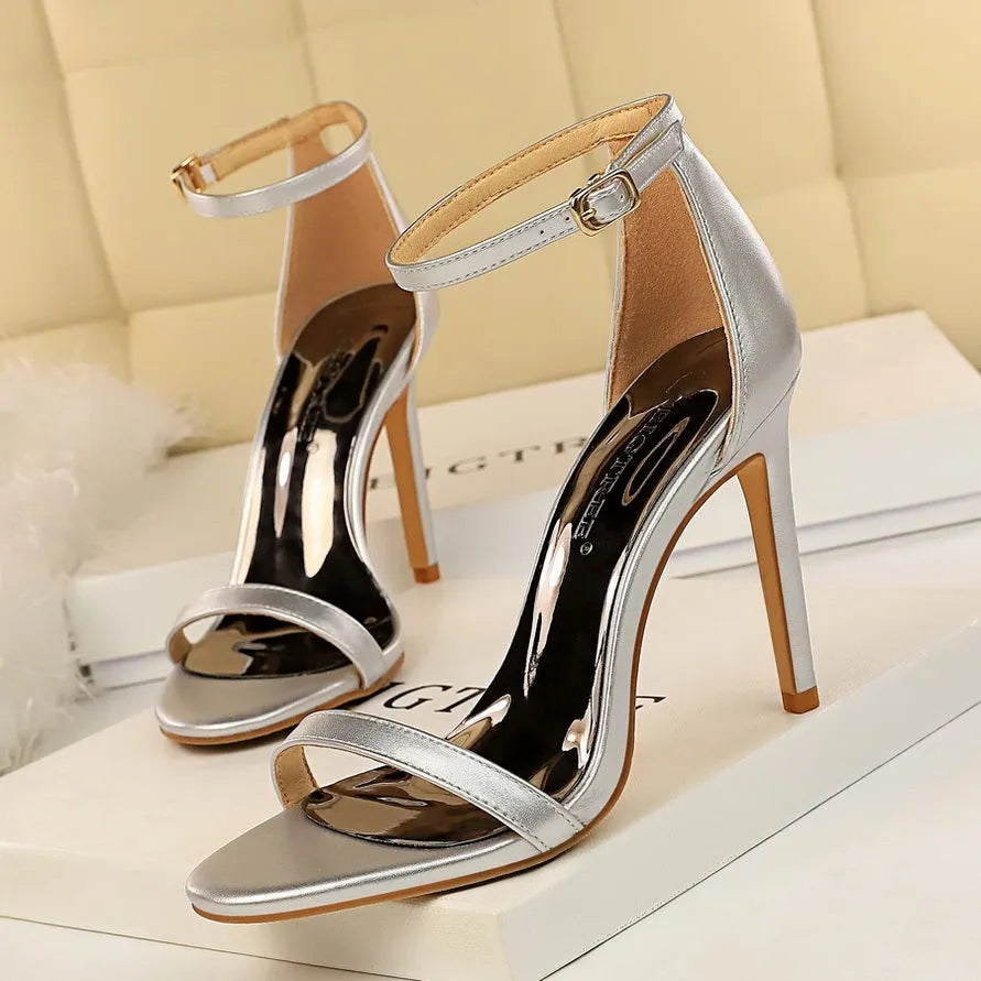 Women's white open-toe high heel sandals with an ankle buckle strap on a plain background.