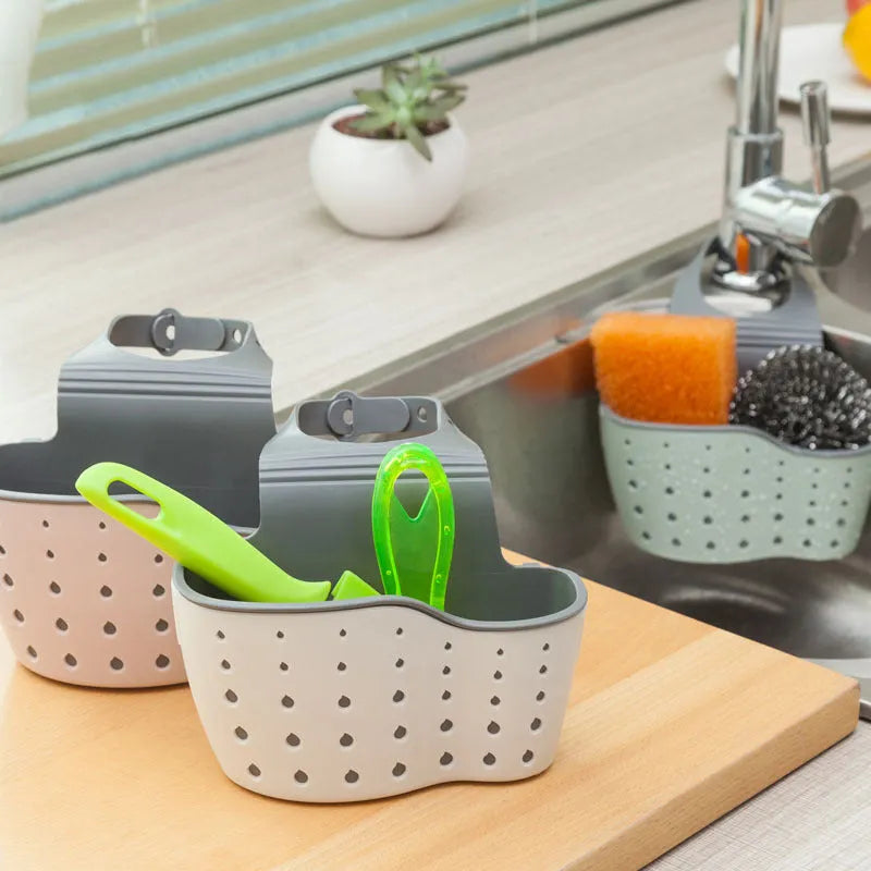 Set of three plastic kitchen sink storage racks in light blue, light pink, and beige on a countertop