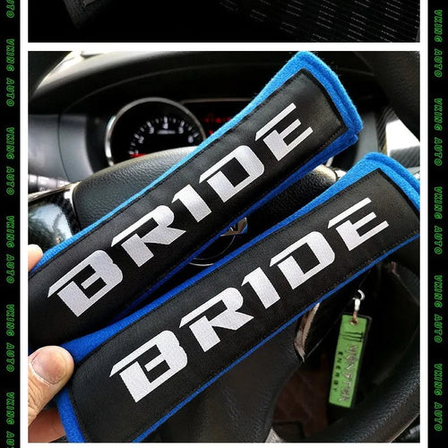 Pair of black cotton seat belt shoulder sleeves with embroidery, shown next to a car seat.