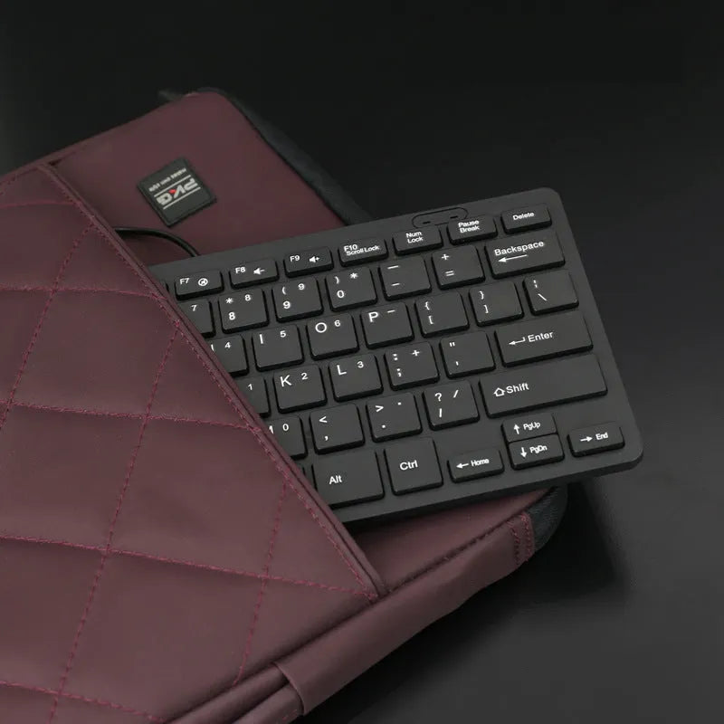 Compact USB wired keyboard in black, white, pink, or blue colour options on a desk.