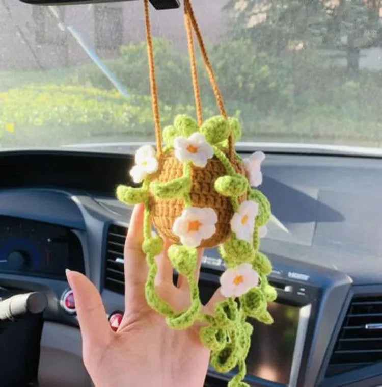 Green and white knitted wool car plant decoration with hanging rope on a car dashboard