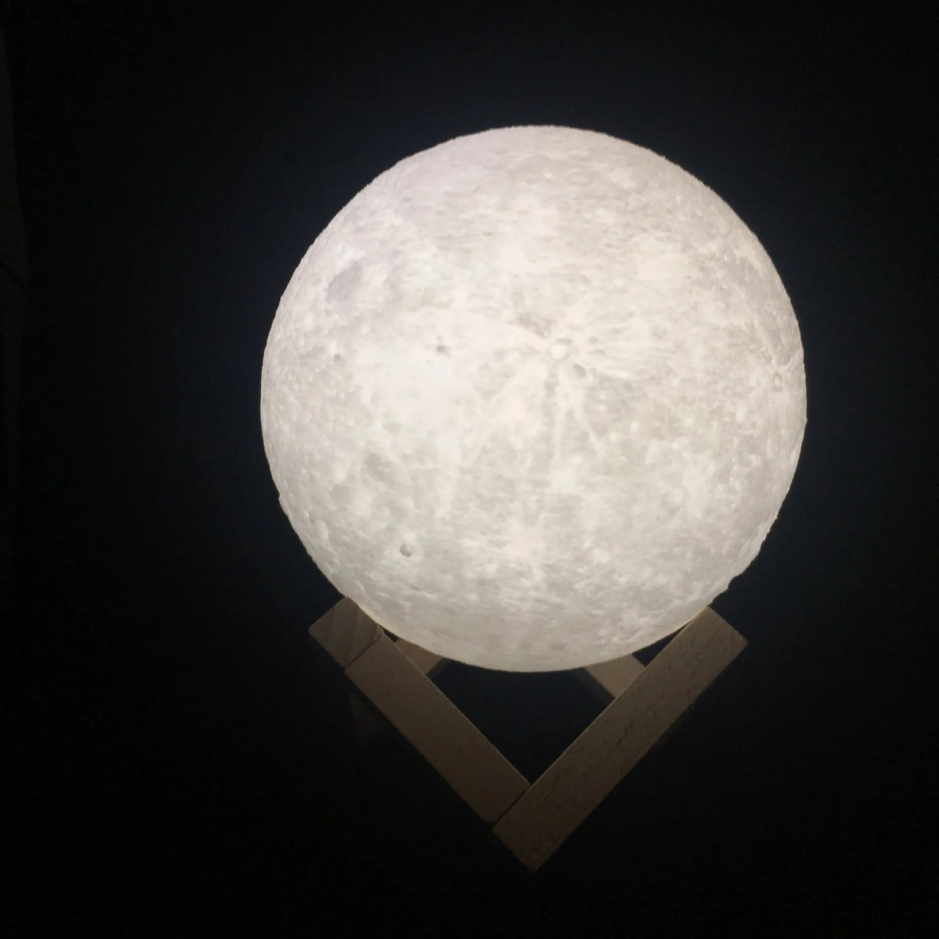 3D printed spherical moon lamp with textured surface on a wooden stand, showing white LED light.