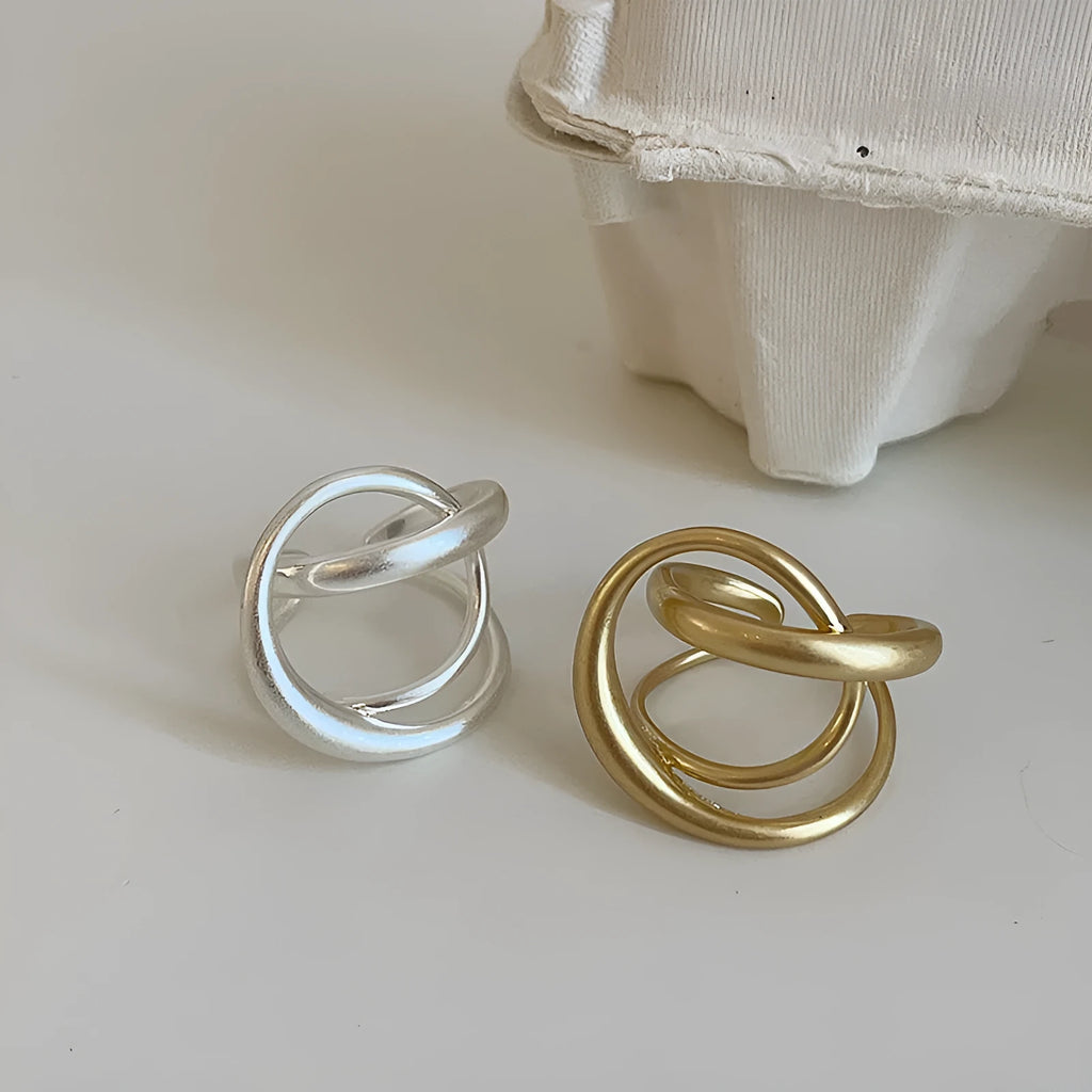 Geometric interlaced open ring with a matte metal finish in gold tone plating.