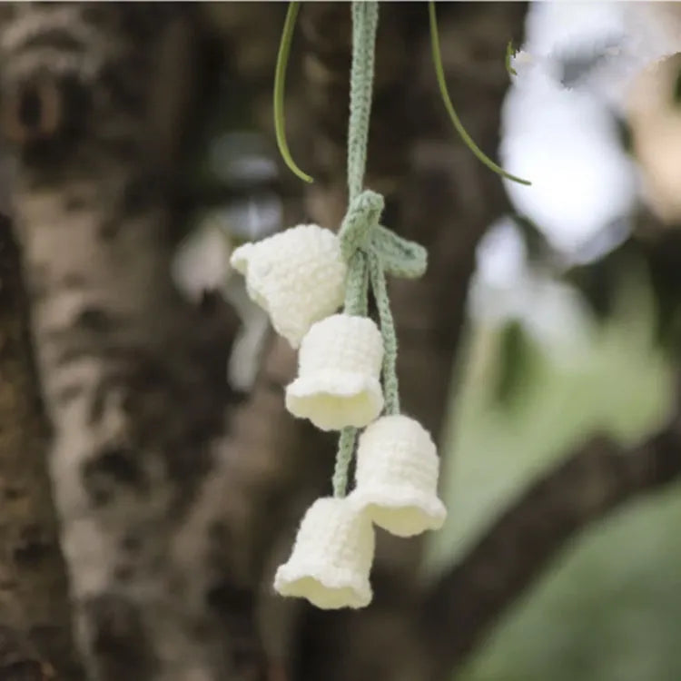 Green and white knitted wool car plant decoration with hanging rope on a car dashboard