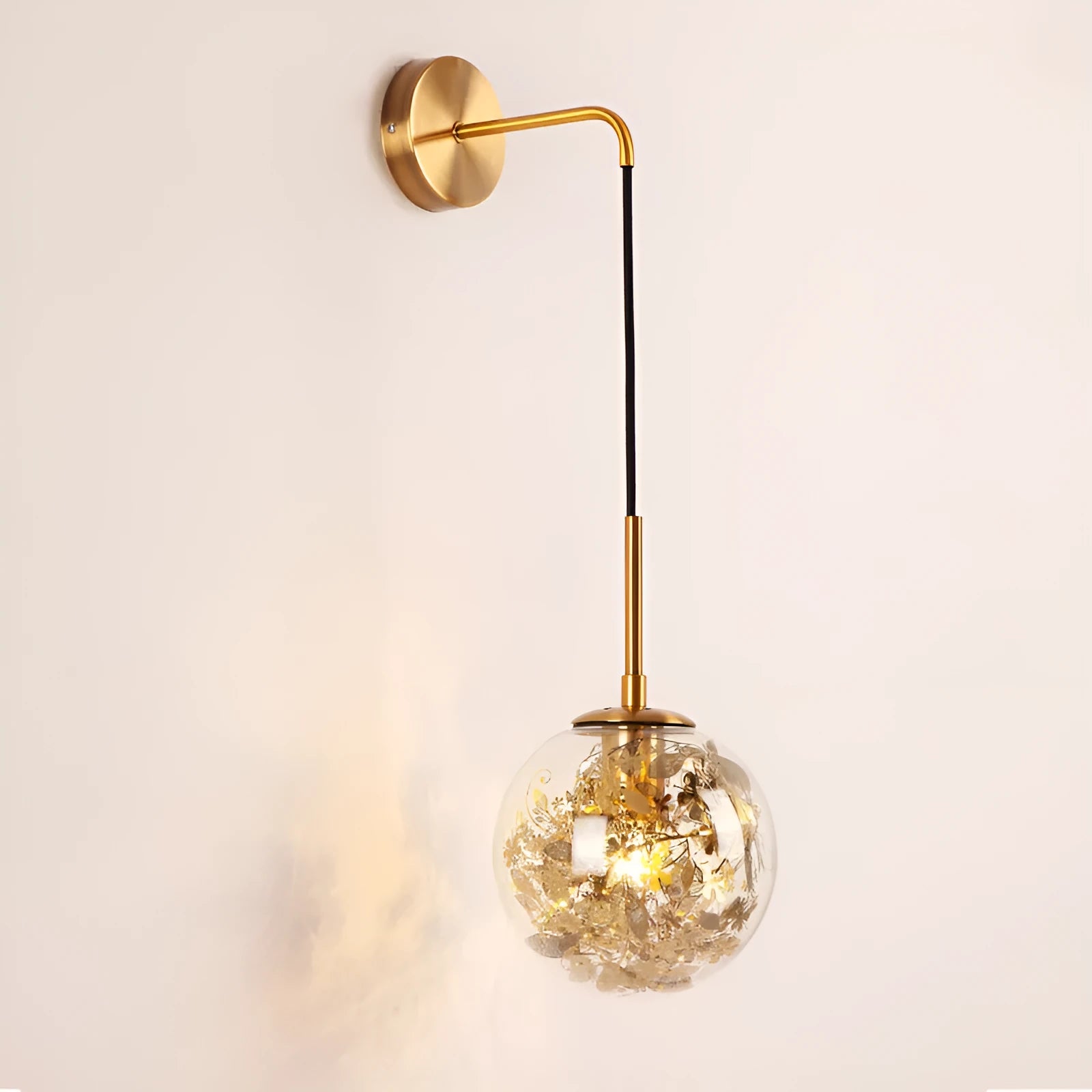 Modern minimalist glass wall lamp with golden flower finish, shown mounted beside a bed.