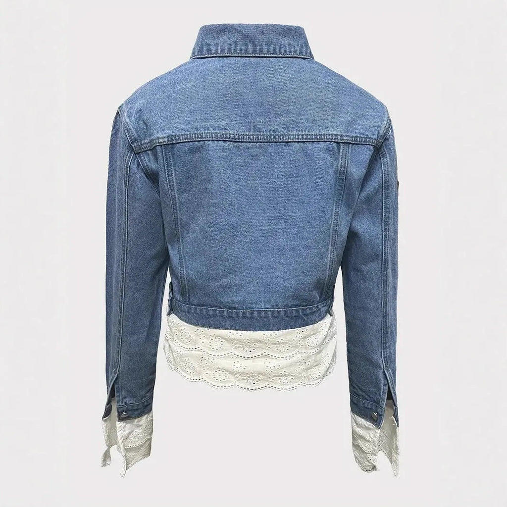 Blue denim jacket for women with lace stitching on the sleeves and front, shown on a hanger.