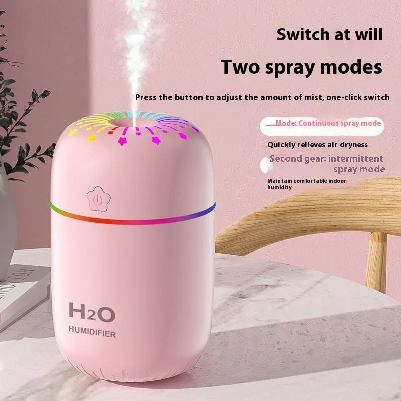 White USB personal mini humidifier with fireworks design on a wooden desk next to a laptop.
