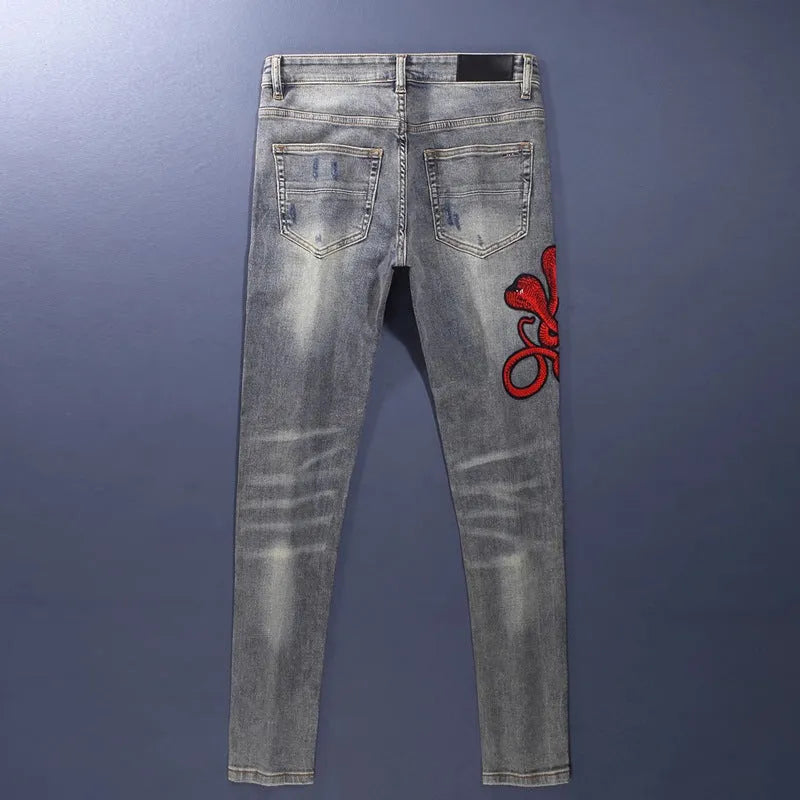 Men's slim fit jeans with a washed-out faded finish and embroidered patch details on the leg.