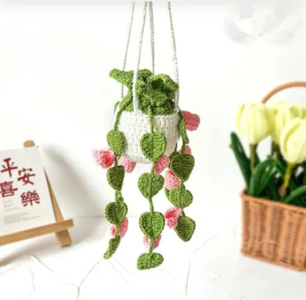 Green and white knitted wool car plant decoration with hanging rope on a car dashboard