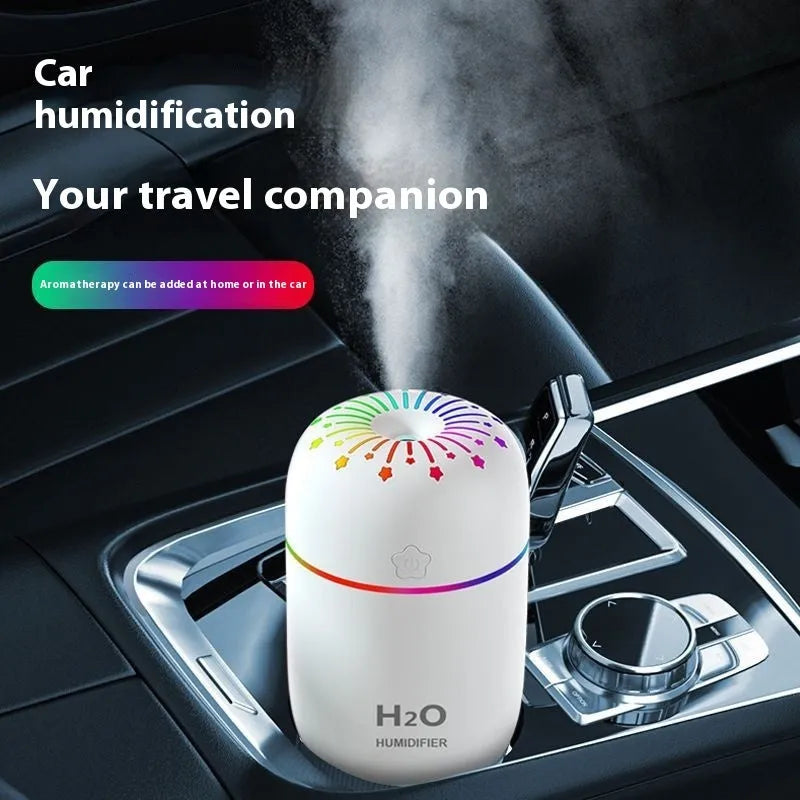White USB personal mini humidifier with fireworks design on a wooden desk next to a laptop.