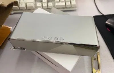 Silver wireless phone charger with clock display, thermometer reading, and integrated mirror on a desk