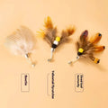 Three steel wire cat toys with small coloured flying insect heads on a table.