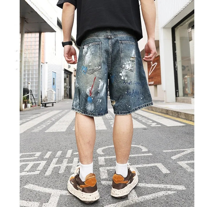 Blue men's ripped denim shorts with graffiti-style detailing and straight-leg cut.