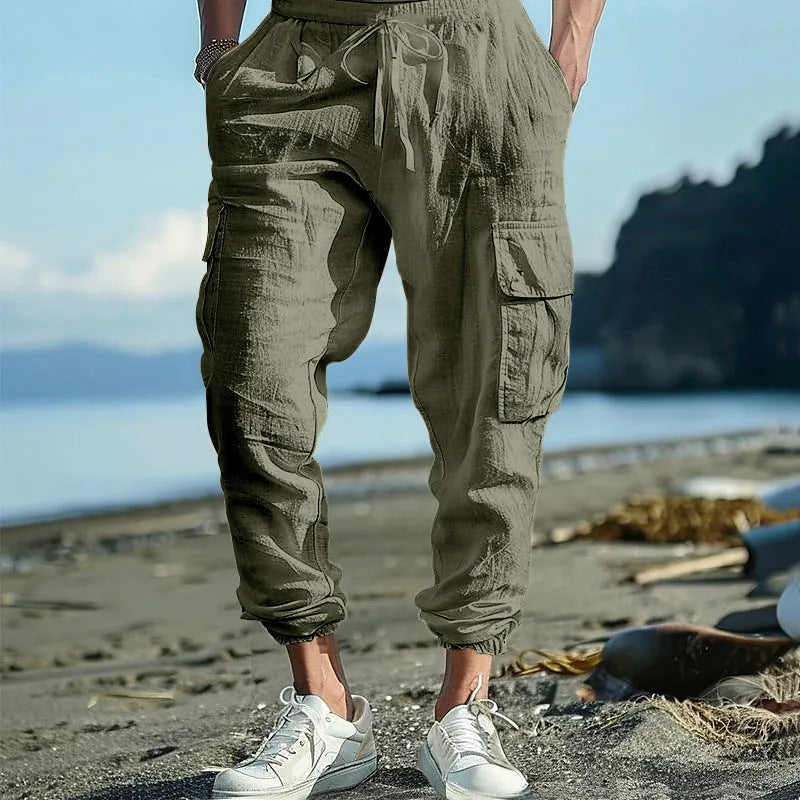 Man wearing loose-fit linen casual trousers with ankle-tied cuffs and multiple pockets in a solid colour.
