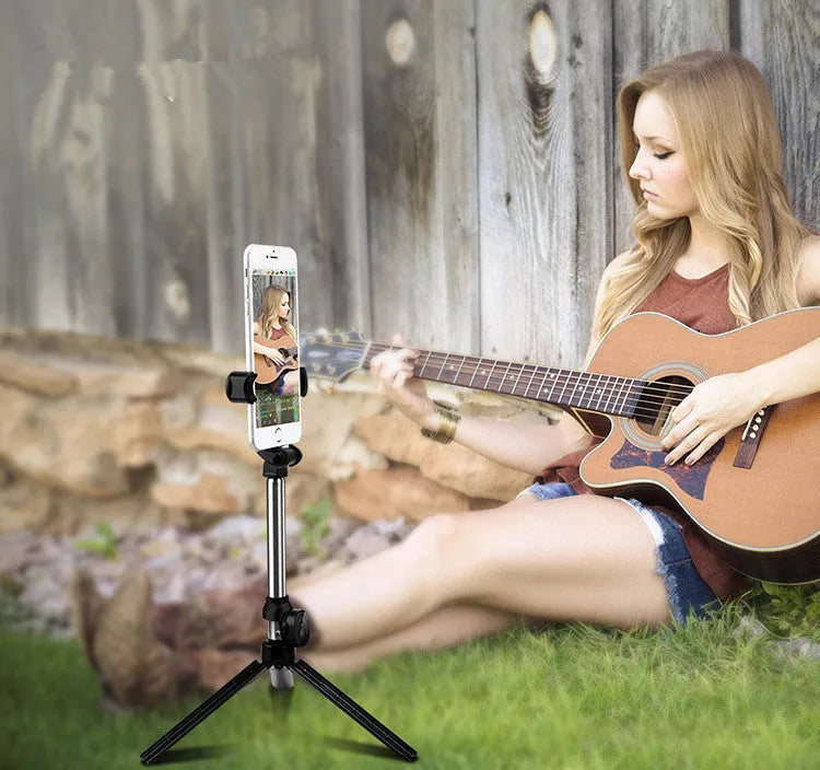 Black Bluetooth selfie tripod with extended stand and 360-degree rotating phone clip attached to an iPhone.