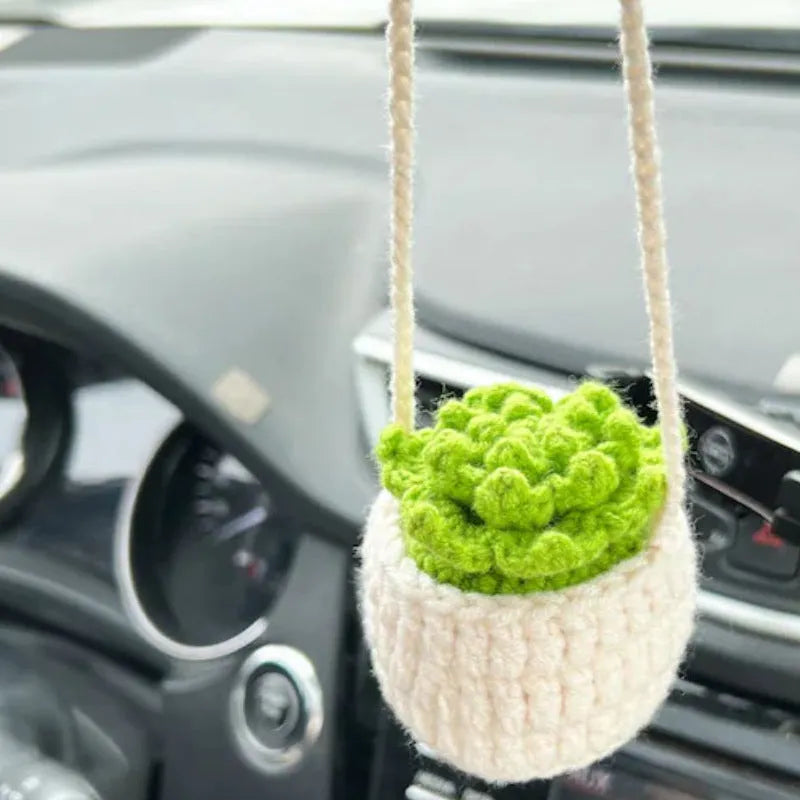 Green and white knitted wool car plant decoration with hanging rope on a car dashboard