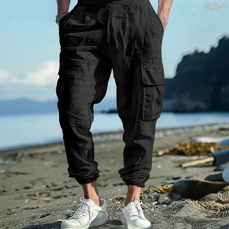 Man wearing loose-fit linen casual trousers with ankle-tied cuffs and multiple pockets in a solid colour.