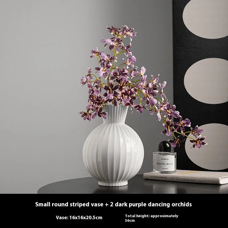 White ceramic ball vase with blue stripes and artificial blue orchid flowers on a wooden table.