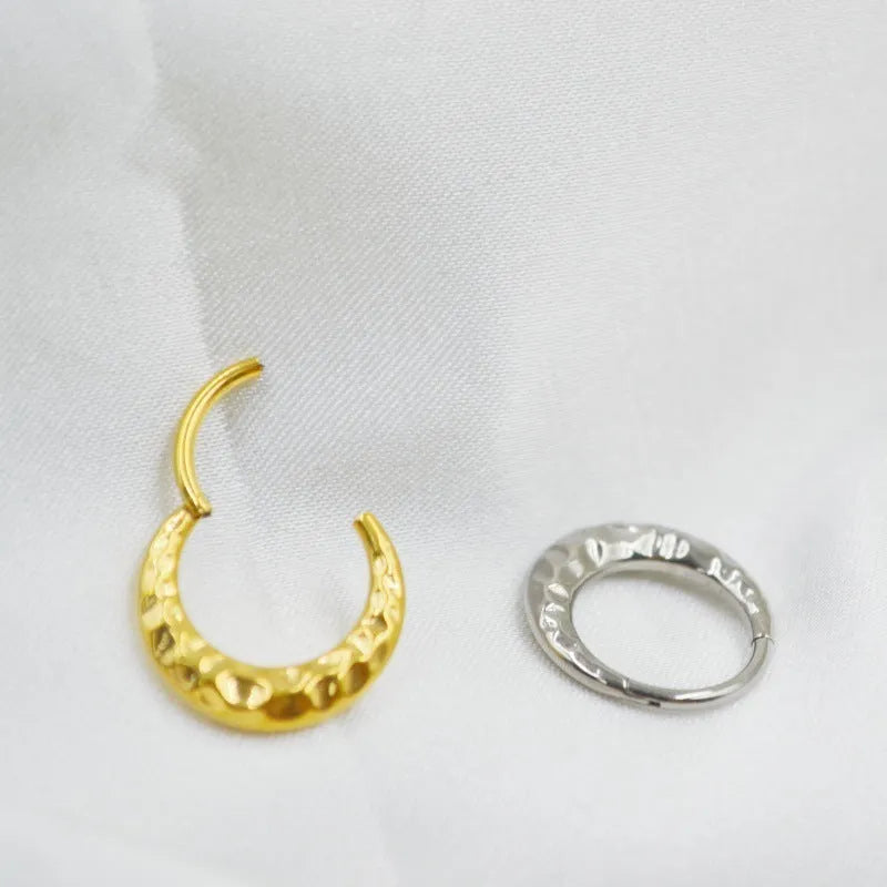 Close-up of a concave-convex titanium nose ring in gold finish on a grey background.