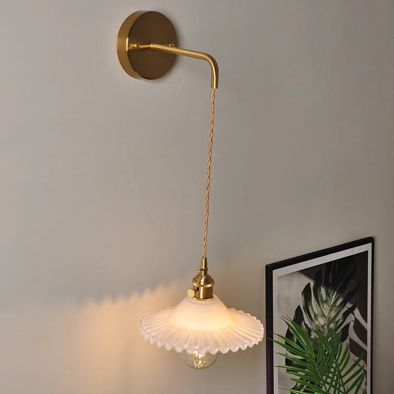 Retro brass copper lotus wall lamp with a glass shade in one of six colours, shown beside a bed.