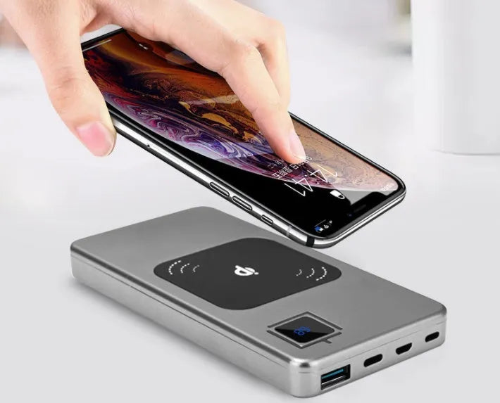 Black portable power bank with LCD display showing battery percentage, next to a smartphone for scale.