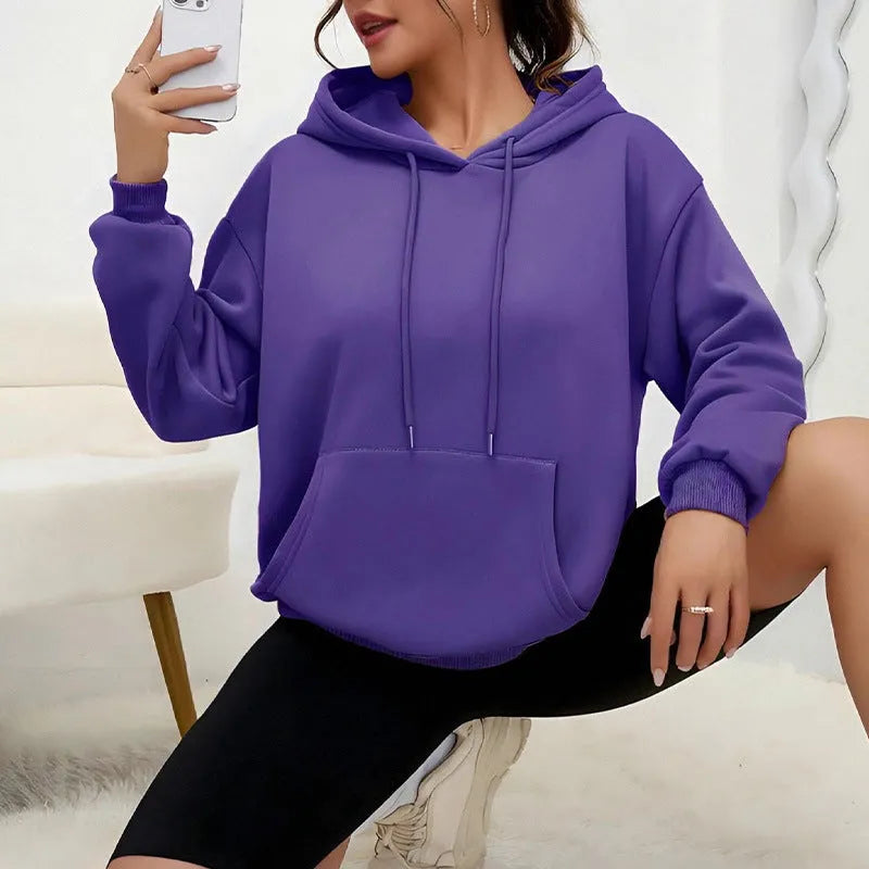 Woman wearing a loose grey drawstring waist sweatshirt with front pockets and long sleeves.