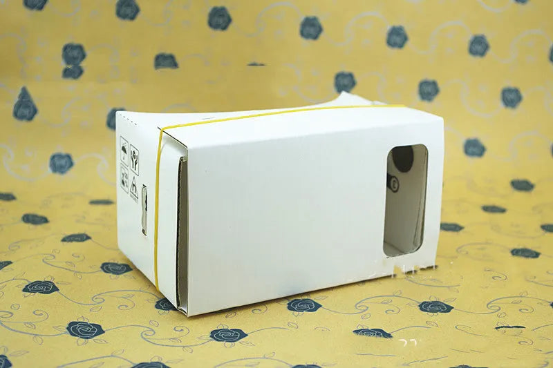 Pink and white cardboard VR glasses headset for smartphones, showing lenses, head strap, and magnetic button.