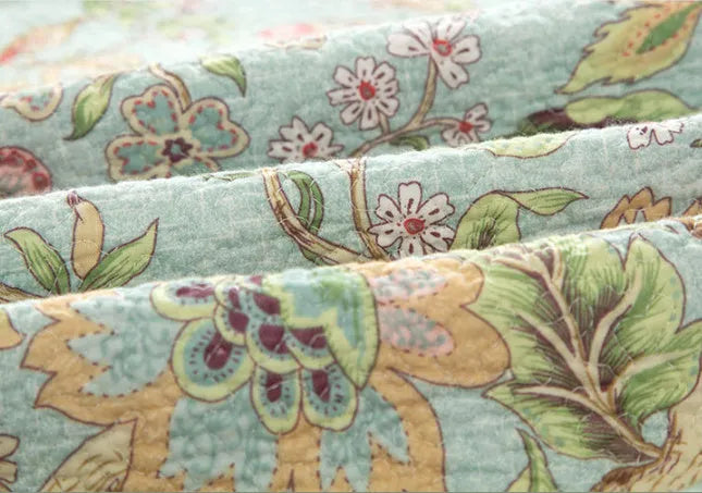 Blue American floral and bird pattern quilted cotton bedspread set of three pieces on a bed.