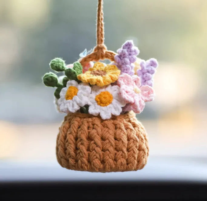Green and white knitted wool car plant decoration with hanging rope on a car dashboard