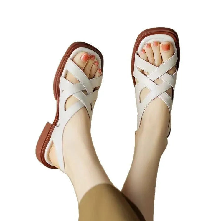 Women's black patent leather square toe sandals with cross strap design on a beach background