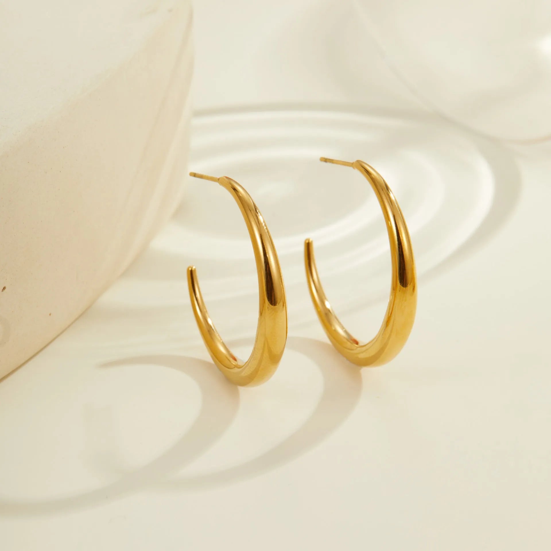A pair of simple round titanium steel hoop earrings in a gold finish on a white background.