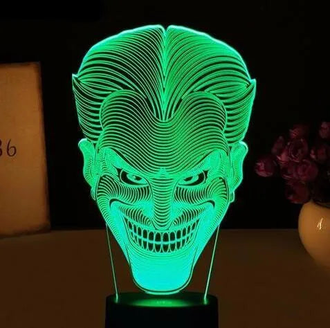 A 3D acrylic LED lamp showing a gradient of colours, sitting on its square base with a remote control nearby.