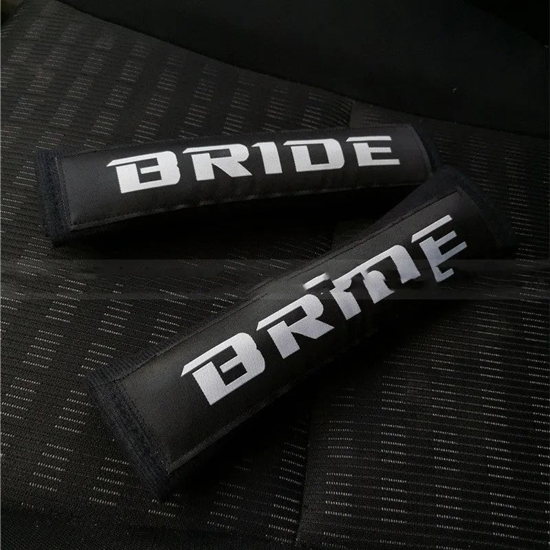 Pair of black cotton seat belt shoulder sleeves with embroidery, shown next to a car seat.