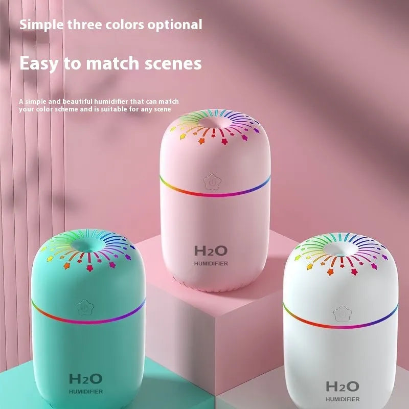 White USB personal mini humidifier with fireworks design on a wooden desk next to a laptop.