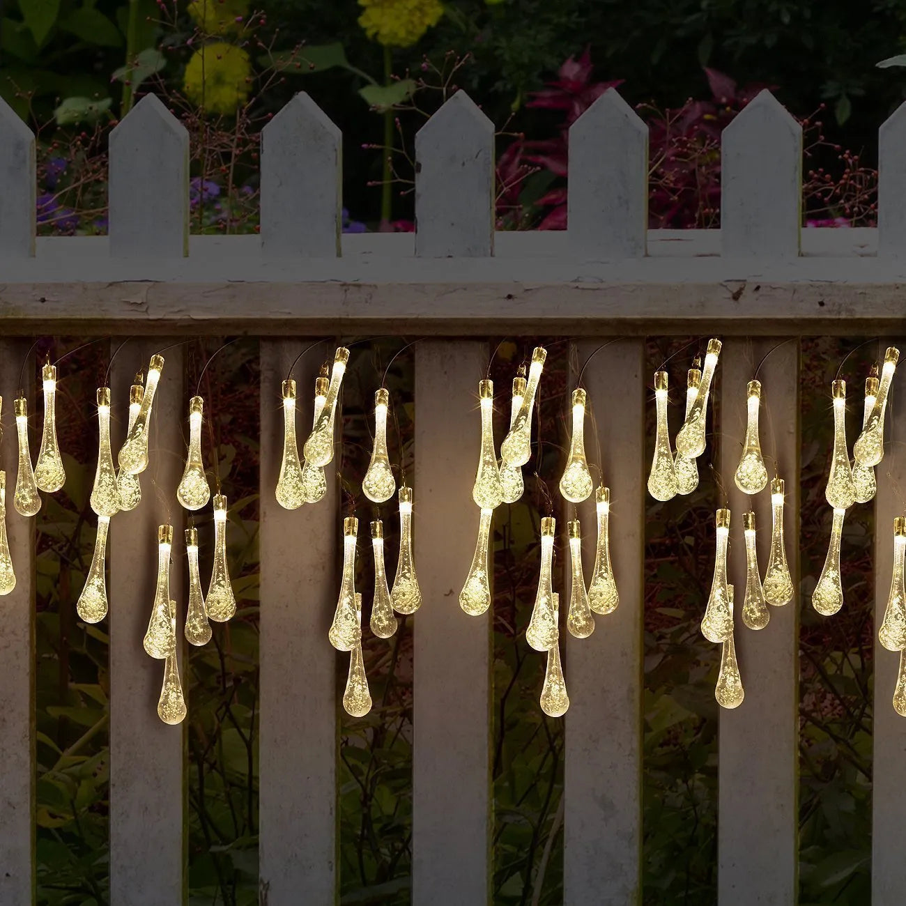 Solar-powered LED outdoor string lights with bubble drop pendants decorating a garden fence