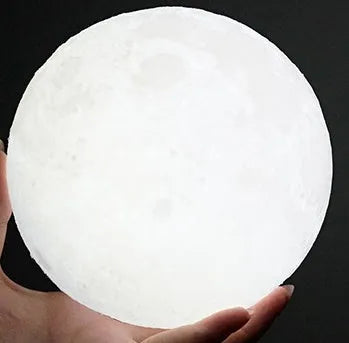 3D printed spherical moon lamp with textured surface on a wooden stand, showing white LED light.
