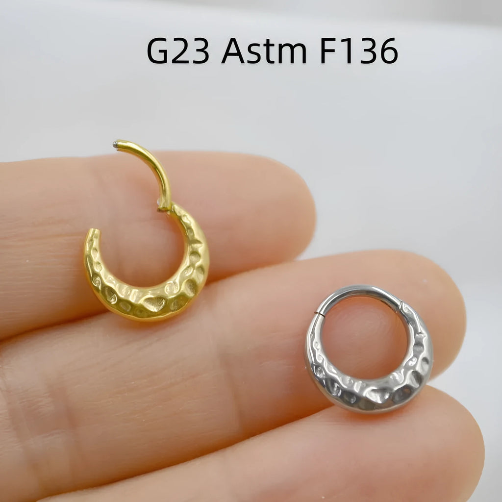 Close-up of a concave-convex titanium nose ring in gold finish on a grey background.