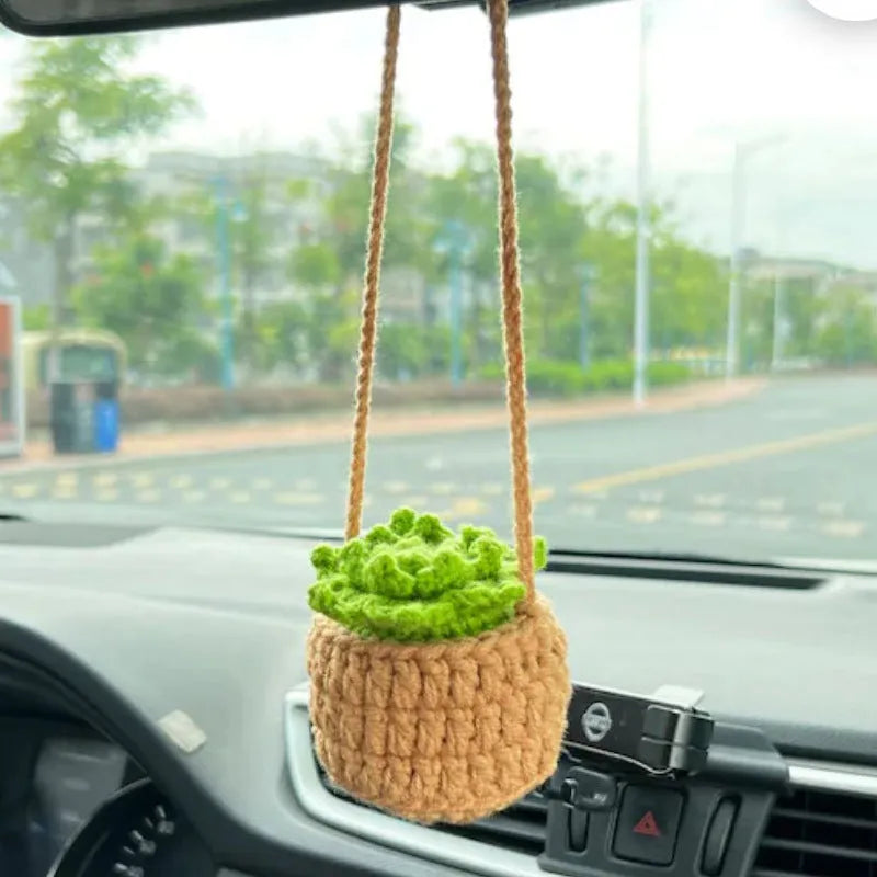 Green and white knitted wool car plant decoration with hanging rope on a car dashboard