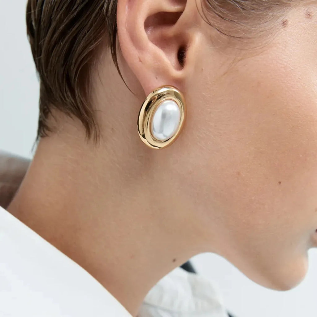 A pair of silver-colour stainless steel stud earrings with a small white pearl detail on a grey background.