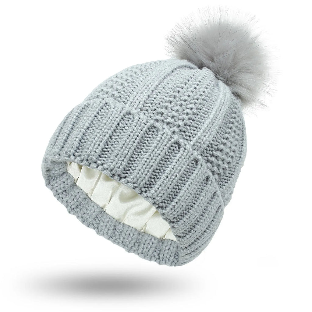 Women's black wool beanie hat with a faux fur pom pom and satin lining on a white background