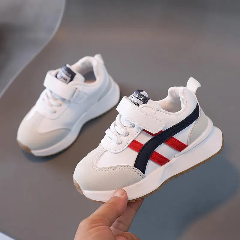 Children's white synthetic leather sneaker with Velcro strap on a neutral background.