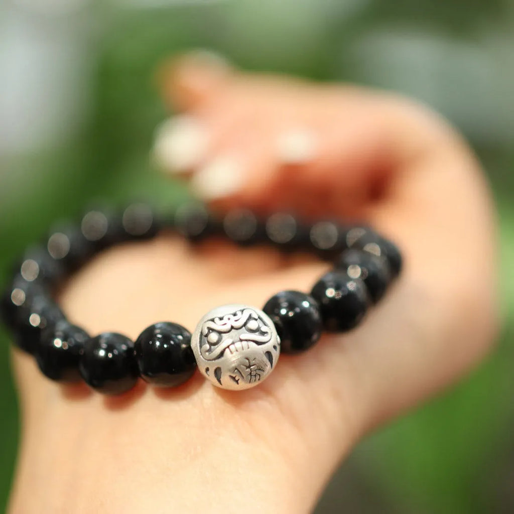 Close-up of a bracelet with large round black agate beads and a sterling silver clasp on a wrist.