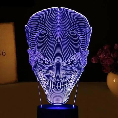 A 3D acrylic LED lamp showing a gradient of colours, sitting on its square base with a remote control nearby.